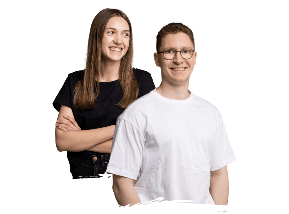 Eine junge Frau und ein junger Mann stehen lächelnd nebeneinander vor einem grünen Hintergrund in Freiburg. Die Frau, schwarz gekleidet, hat die Arme verschränkt, während der Mann in Weiß steht